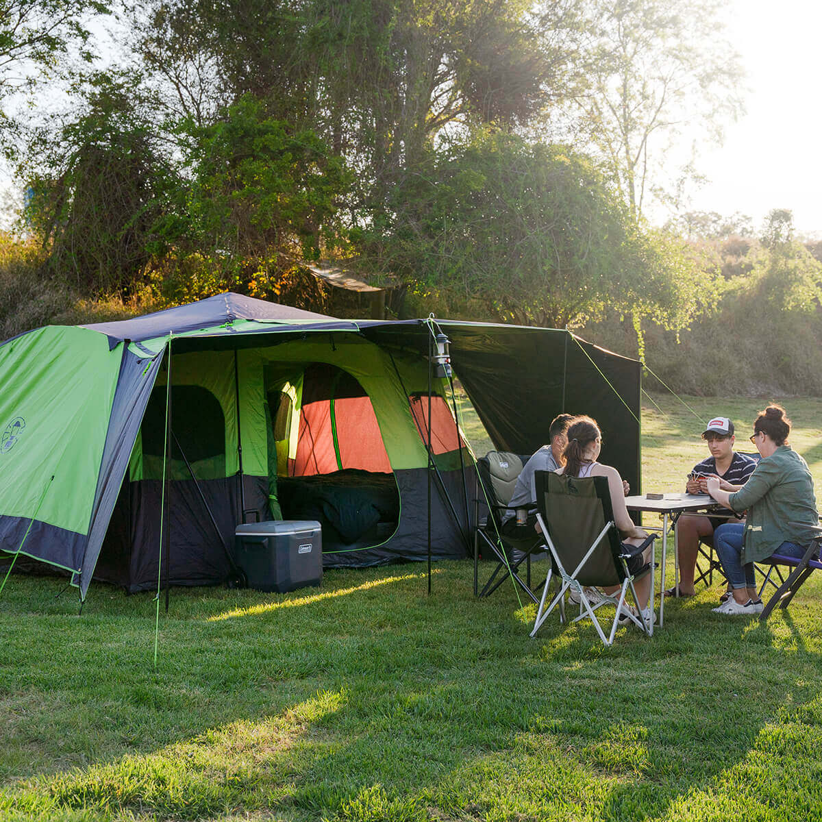 Pitched at a campsite with awning and sunwalls up, group of 4 playing cards at a table in front of the tent