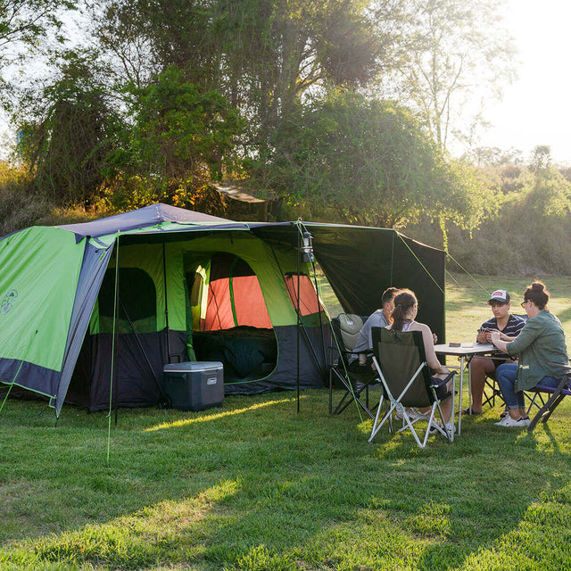 Pitched at a campsite with awning and sunwalls up, group of 4 playing cards at a table in front of the tent