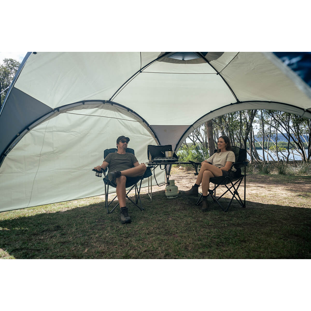 View showing interior of an Event 12 Deluxe Shelter with the sunwall attached and a couple sitting in front of it with a stove on a table