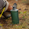 Sage Green, photo of full bottle beside owner sitting on the ground