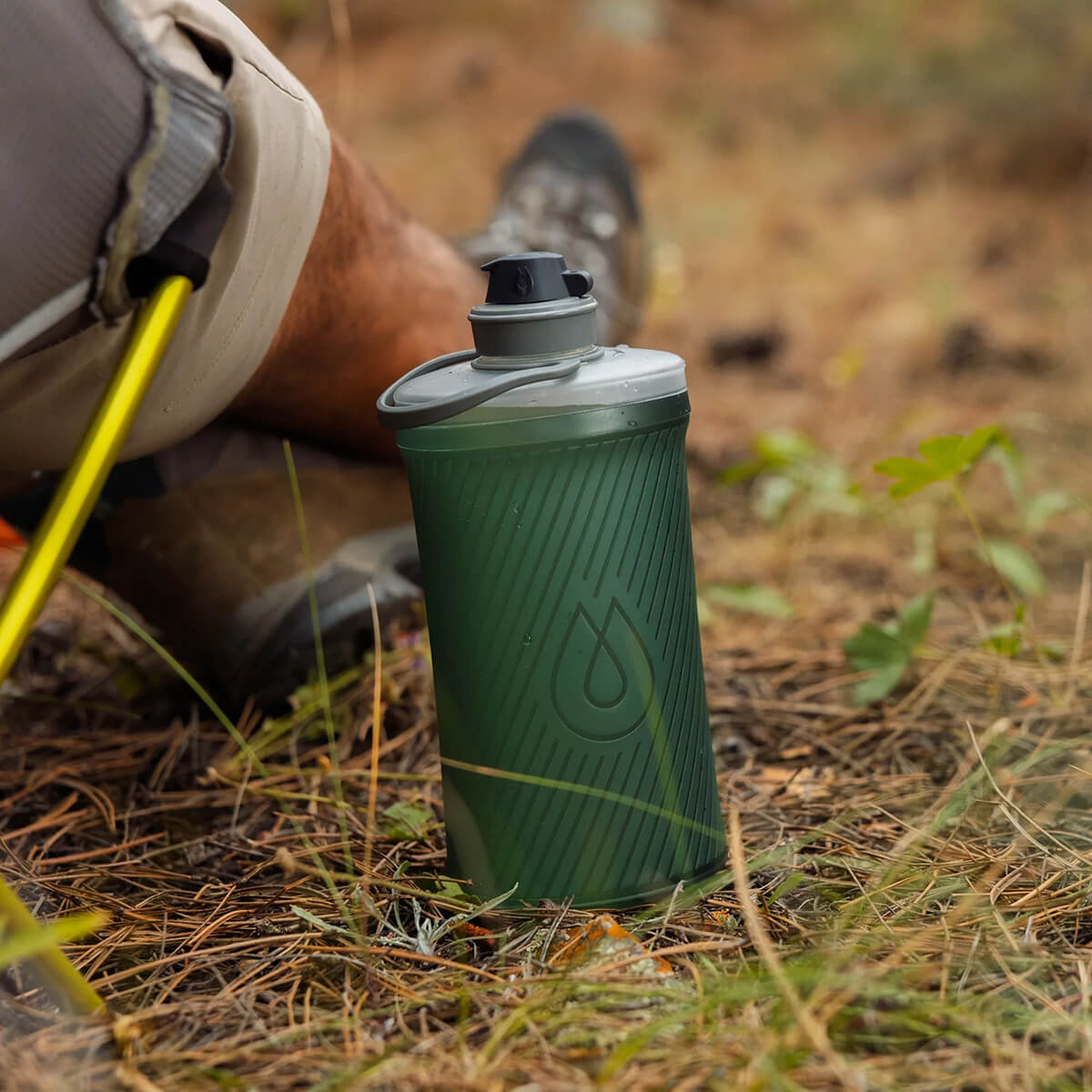 Sage Green, photo of full bottle beside owner sitting on the ground